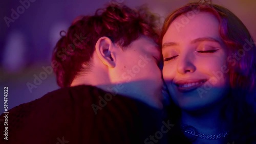 Close-up of a sensual couple flirting, kissing under neon lights in a nightclub. The couple drinks alcohol and kisses. Night club