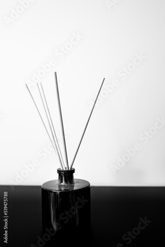 Aromatic sticks in a black ceramic vase. Interior objects still life in monochromatic colors on the black table against a white wall backdrop.