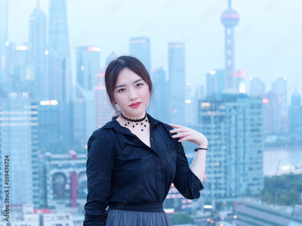 Beautiful young Chinese woman in black posing on top of mansion roof with blur Shanghai Bund landmark buildings background with dusk light. Emotions, people, beauty and lifestyle concept. Beautiful young Chinese woman in black posing on top of mansion roof with blur Shanghai Bund landmark buildings background with dusk light. Emotions, people, beauty and lifestyle concept.