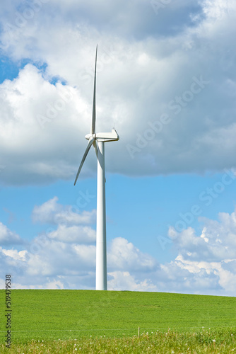 Windmill. A windmill on a green hill against cloudy blue sky with copy space. Wind turbines generate electricity through spinning propeller blades. Conceptual nature scene for renewable energy.