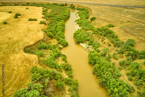 a winding muddy river with overgrown green banks in a sun-scorched steppe rural landscape © сергей тарануха