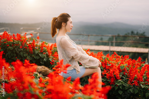 Rear view image of a female traveler sitting and looking at a beautiful mountain,flowerr field and nature view. photo