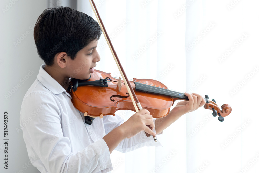 Indian boy practicing playing violin at home, holds the violin instrument beside the window, creative children play song, classical education Indian boy practicing playing violin at home, holds the violin instrument beside the window, creative children play song, classical education
