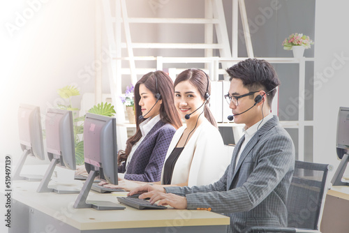 Side view of young asian operator man and woman in headsets using laptops while working in office. Middle womean looking at camera. Concept of call center service for business.