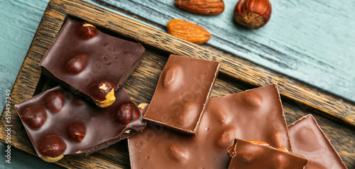 Pieces of tasty chocolate with hazelnuts and almonds on wooden table, closeup