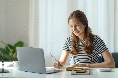 Beautiful young Asian woman student studying online with laptop computer at home.