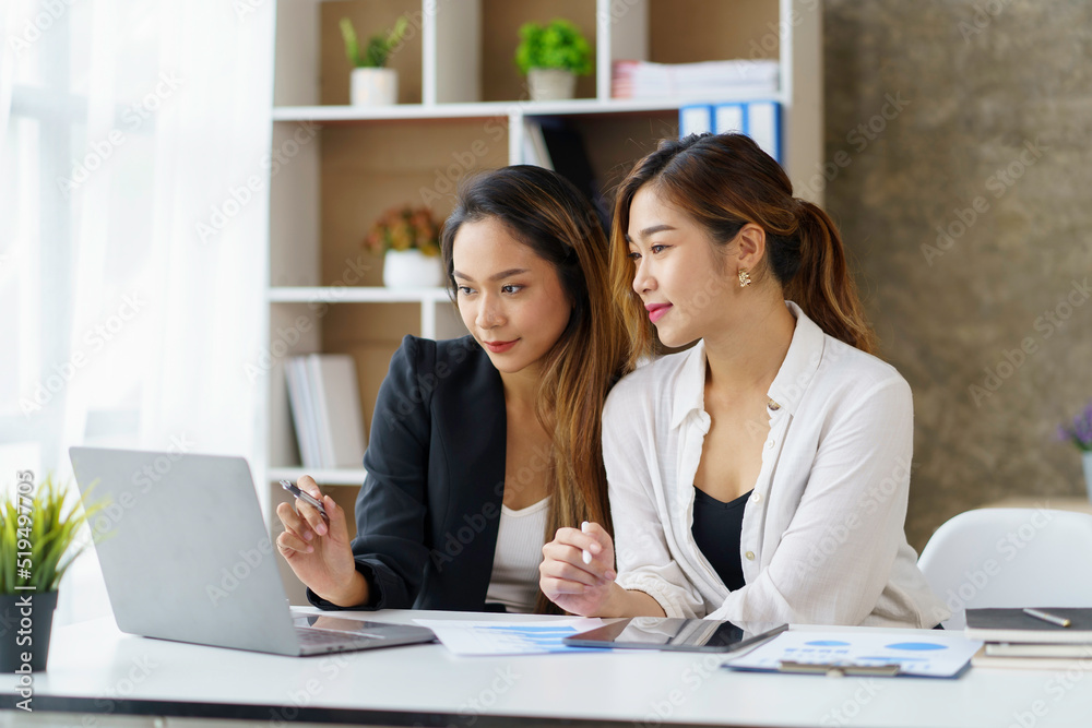 Two professional Asian business women discuss work using a laptop computer to work in the office. Two professional Asian business women discuss work using a laptop computer to work in the office.