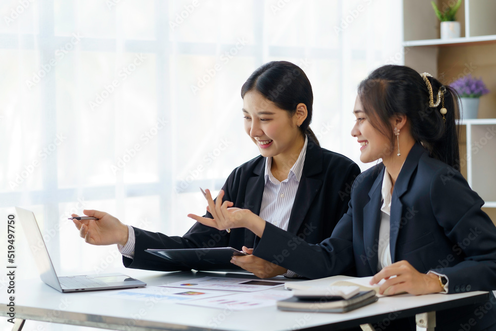 Two professional Asian business women discuss work using a laptop computer to work in the office. Two professional Asian business women discuss work using a laptop computer to work in the office.