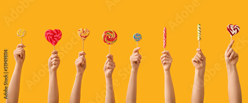 Many hands with sweet lollipops on yellow background