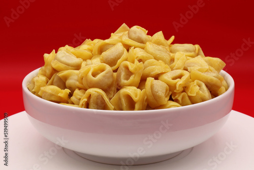 Raw Tortellini Pasta in a bowl isolated on red background. Traditional Italian pasta