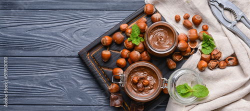 Fotografie, Obraz Jars with tasty chocolate paste and hazelnuts on dark wooden background, top vie