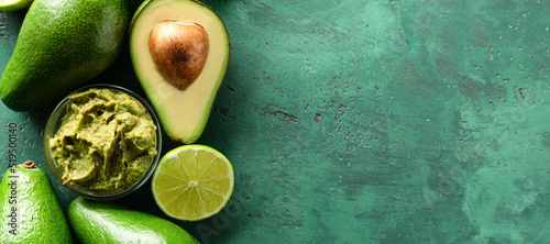 Bowl with delicious guacamole, lime and ripe avocados on green background with space for text