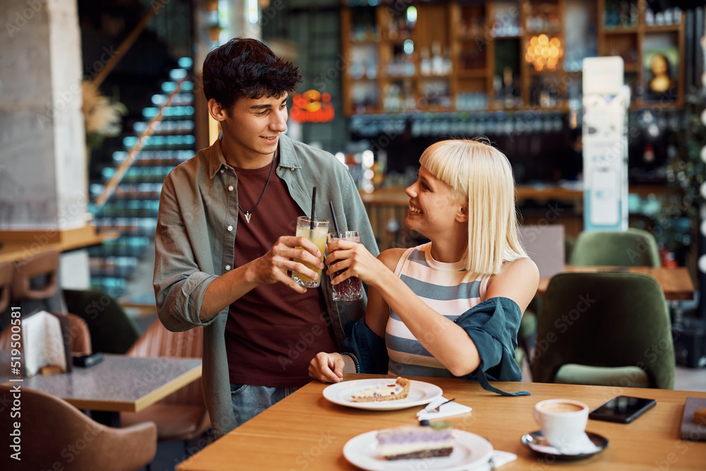 Young couple having fun and toasting with juices while eating dessert in cafe.