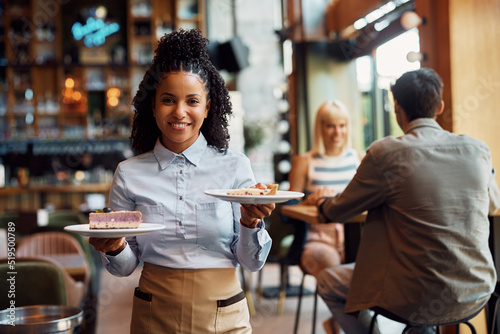 Happy black waitress serving dessert in a cafe and looking at camera. photo