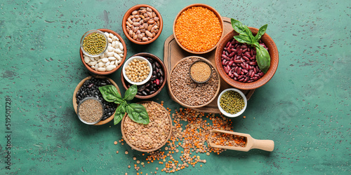 Different raw legumes with spices on green background