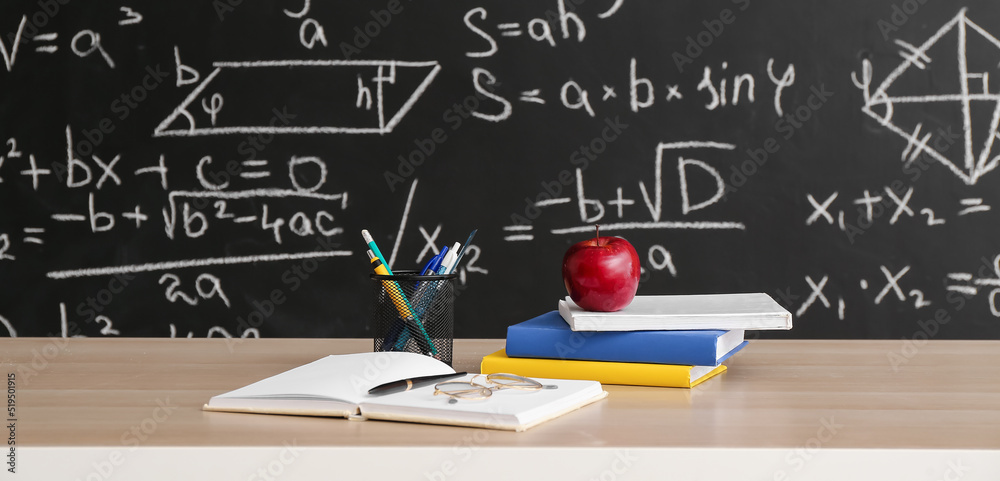 Apple with books and school stationery on table in classroom Apple with books and school stationery on table in classroom