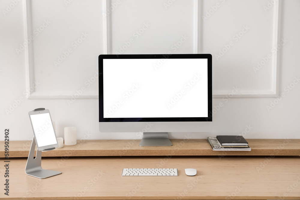 Modern workplace with computer and tablet near light wall Modern workplace with computer and tablet near light wall