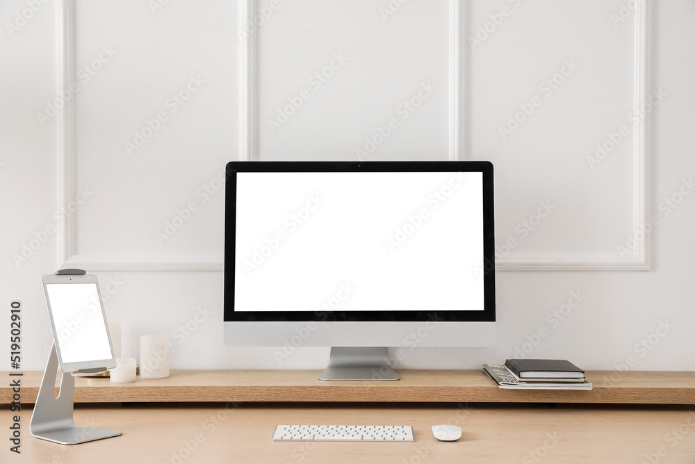 Modern workplace with computer and tablet near light wall