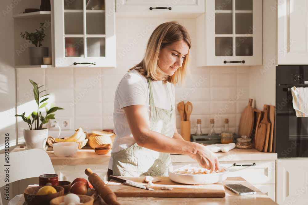 charming young woman in chef's apron preparing pie at home in the kitchen Cozy home interior charming young woman in chef's apron preparing pie at home in the kitchen Cozy home interior