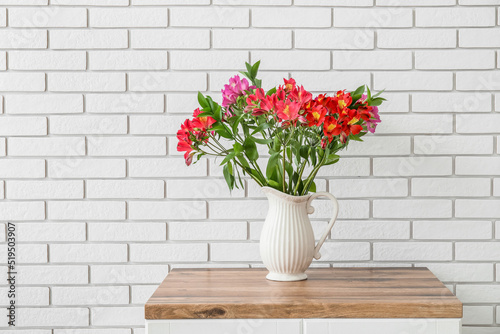 Vase with beautiful alstroemeria flowers on table against brick wall