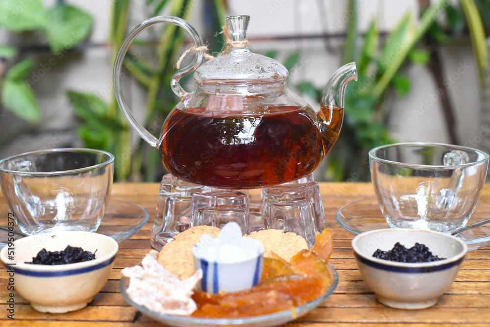 Earl Grey tea in a glass teapot with cups and crystalized fruits on wooden table Earl Grey tea in a glass teapot with cups and crystalized fruits on wooden table