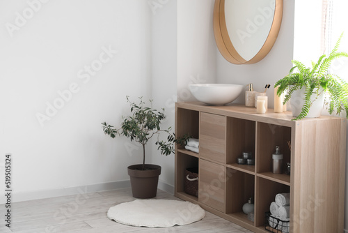Wooden shelving unit with sink and bath accessories near light wall