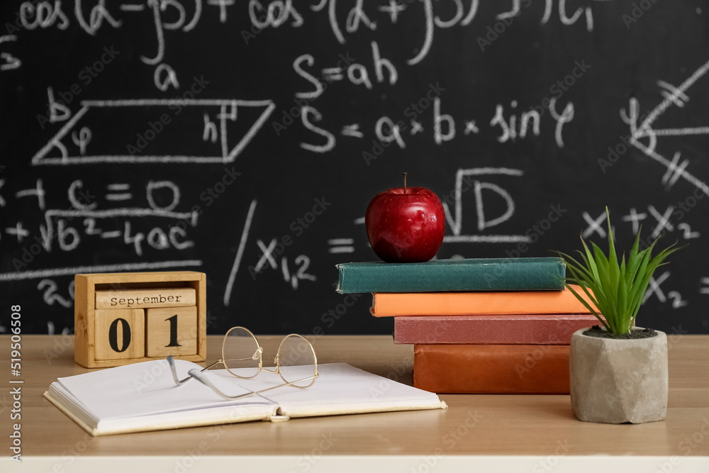 Cube calendar with date 1 SEPTEMBER, apple, books and eyeglasses on table near blackboard Cube calendar with date 1 SEPTEMBER, apple, books and eyeglasses on table near blackboard