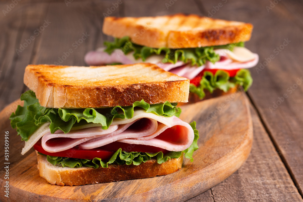 Close-up of two toasted sandwiches with fresh ham, cheese and vegetables on background. Club sandwich and take-away concept. Fast food. Close-up of two toasted sandwiches with fresh ham, cheese and vegetables on background. Club sandwich and take-away concept. Fast food.