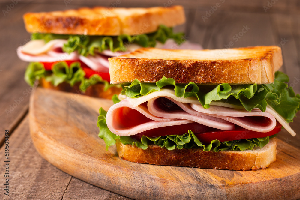 Close-up of two toasted sandwiches with fresh ham, cheese and vegetables on background. Club sandwich and take-away concept. Fast food. Close-up of two toasted sandwiches with fresh ham, cheese and vegetables on background. Club sandwich and take-away concept. Fast food.