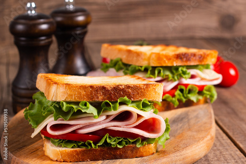 Close-up of two toasted sandwiches with fresh ham  cheese and vegetables on background. Club sandwich and take-away concept. Fast food. 