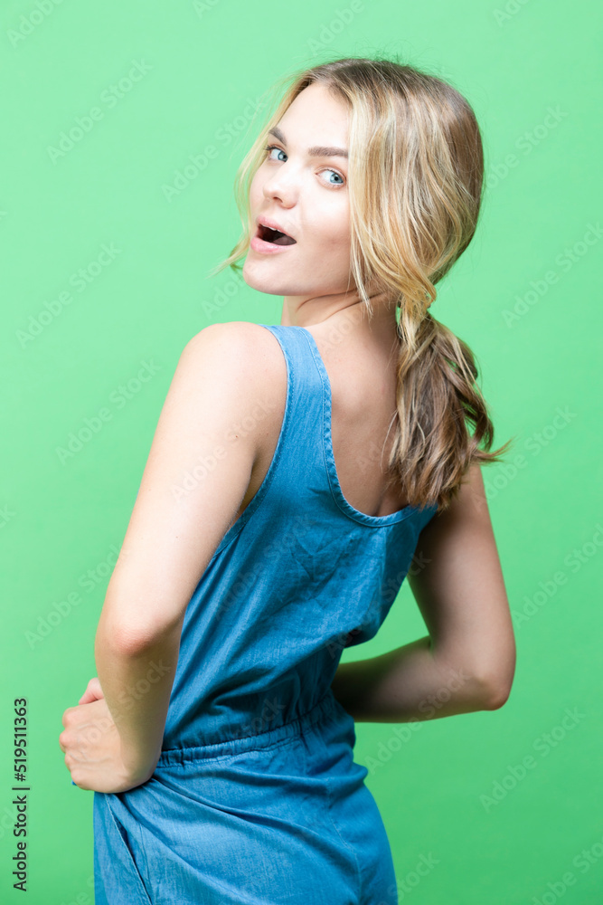 Winsome Caucasian Blond Girl In blue suite Posing In Summer outfit While looking Backwards With Positive Expression Over Summer Green Background. Winsome Caucasian Blond Girl In blue suite Posing In Summer outfit While looking Backwards With Positive Expression Over Summer Green Background.