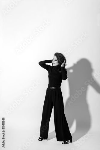 Beauty, fashion, style and make-up concept. Beautiful woman with dark pants and blouse studio portrait. Girl making various fashion poses. Model with long dark and wavy hair. Black and white image