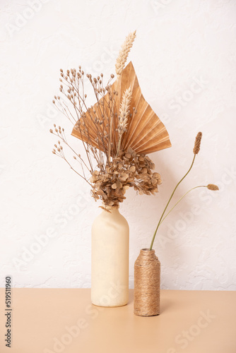 A bouquet of beige flowers and paper palm trees on white wall background