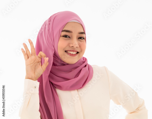 Beautiful and smiling young muslim woman presenting OK hand gesture or hand signal isolated on white background. Concept of confirmaing sign, surely signal