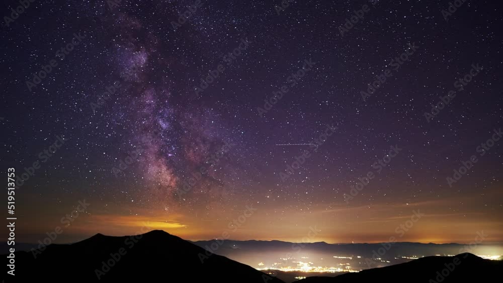 The core of the milkyway in the night sky,the silhouette of the hills and glowing city in the valley