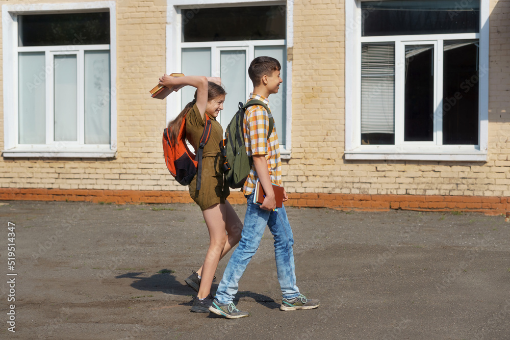 schoolchildren are having fun in the school yard - a teenage girl wants to hit a boy on the head with books