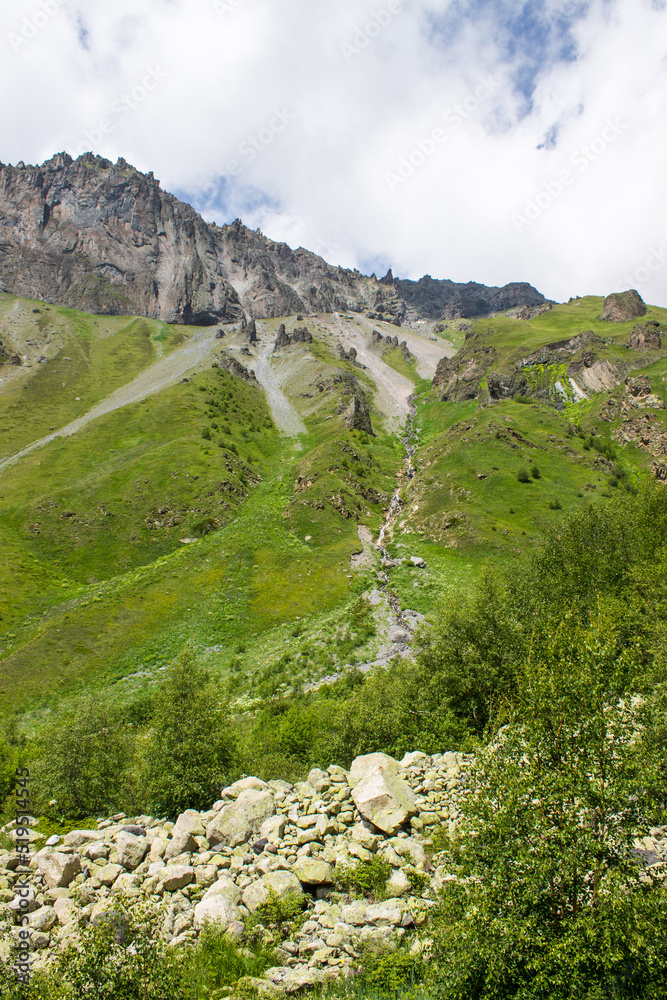Obraz premium Beautiful landscape - green hills in the terskol valley with bright grass and high gray rocks with sharp peaks and stones on a clear summer sunny day near elbrus russia