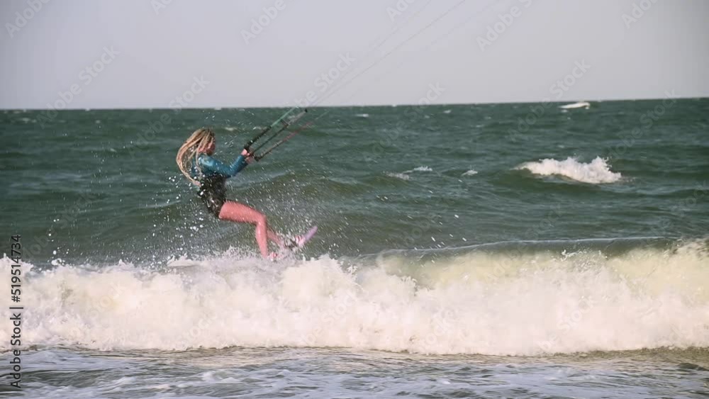 Young adult caucasian woman in good shape enjoys riding a kiteboard for surfing, doing extreme tricks on a bright sunny windy day Young adult caucasian woman in good shape enjoys riding a kiteboard for surfing, doing extreme tricks on a bright sunny windy day