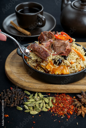 rice pilaf with meat in a round pan on a board with a fork in female hands 