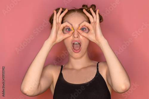 A beautiful shocked and surprised girl with braces holds her hands near eyes and opened mouth looks at the camera with surprise and joy. Concept of omg discounts, sale, gifts.