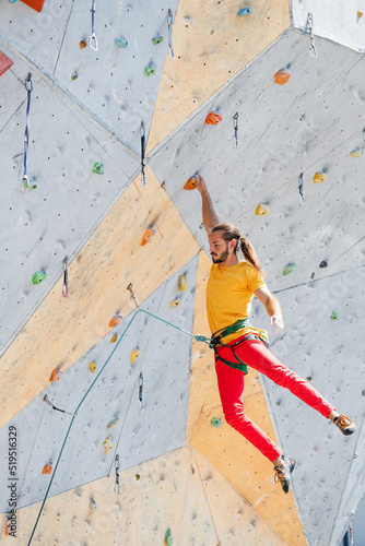Sportsman climber hanging with one hand on an artificial climbing wall outdoors.