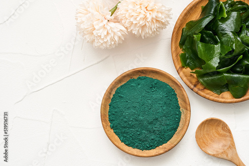top view or flat lay laminaria or kelp seaweed and spirulina powder in wood plate and spoon background. spirulina powder with konbu and alga food on white table background.                        