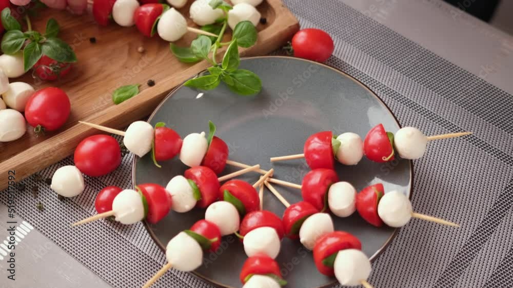 putting caprese canapes with cherry tomatoes and mozzarella cheese balls on a plate putting caprese canapes with cherry tomatoes and mozzarella cheese balls on a plate