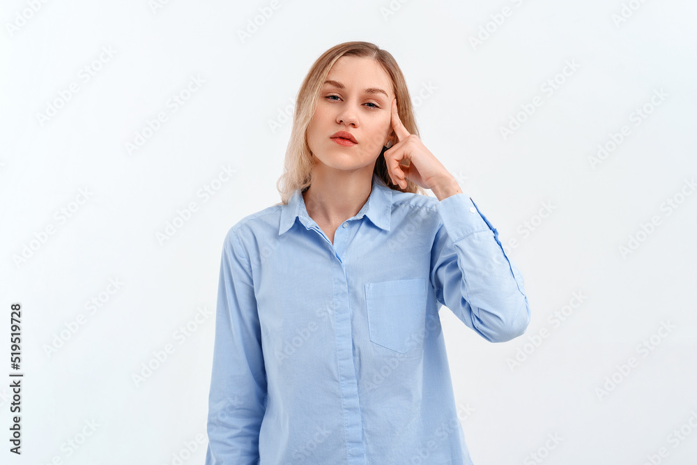 Young serious blonde woman points to head with one finger, great idea or thought, good memory, stands in blue shirt. Indoor studio shot on white background. Think about it Young serious blonde woman points to head with one finger, great idea or thought, good memory, stands in blue shirt. Indoor studio shot on white background. Think about it