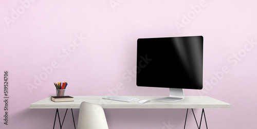 Blank computer display on work desk with pens and book beside. Pink wall in background © Stanisic Vladimir