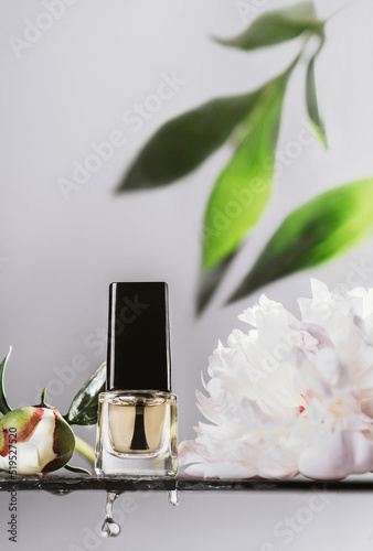 clear nail polish. nail polish in a transparent glass bottle. nail oil in a transparent bottle on a background of white peonies. cosmetics and peonies. nail polish and water splash