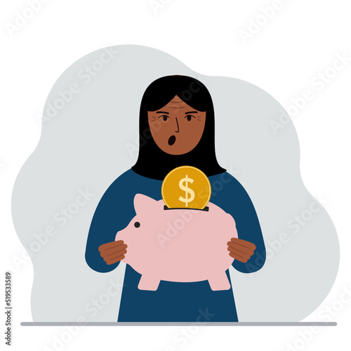 Happy muslim woman holds a piggy bank, a coin falls into the piggy bank. The concept of saving finance, savings, investing finances.