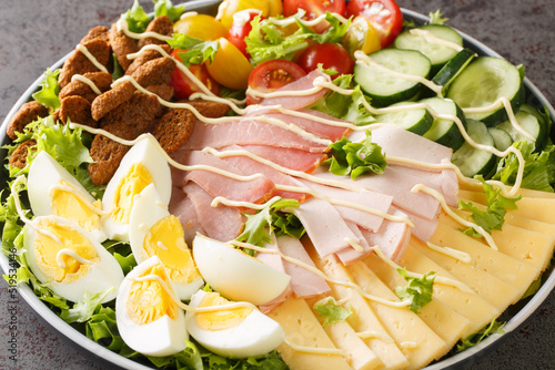 Classic chef salad is a greens salad that is served with assorted meats, cheese, and vegetables and coasted in a homemade dressing closeup in the plate on the table. Horizontal