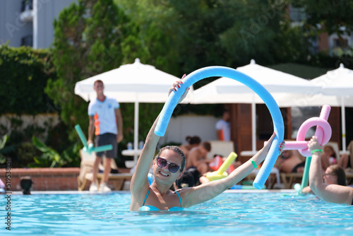 Fototapeta Naklejka Na Ścianę i Meble -  Attractive smiling woman in sunglasses using swimming noodles in pool