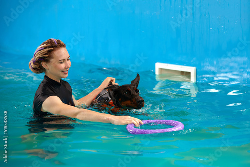 Schilderij op canvas Dog in life jacket swim in the swimming pool with coach